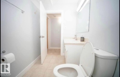 Bathroom featuring a white toilet, tile flooring, wall-mounted mirror, and vanity with an integrated sink - 10139 74 Street Nw, Edmonton, AB 