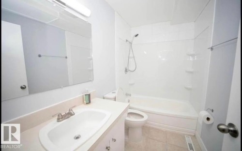 Vanity with integrated sink, chrome faucet, and expansive mirror with overhead lighting - 10139 74 Street Nw, Edmonton, AB 