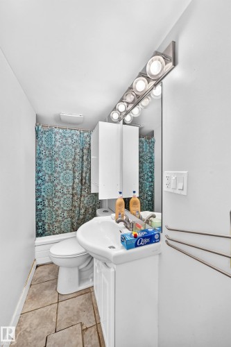 Compact bathroom featuring a white vanity with integrated sink, a rectangular mirror, and overhead strip lighting - 10139 74 Street Nw, Edmonton, AB 