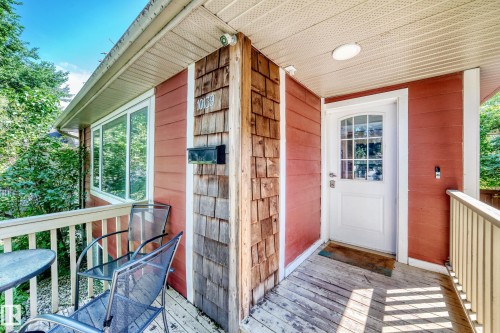 Front porch with wood decking, white railings, and a white paneled door with glass inserts - 10139 74 Street Nw, Edmonton, AB 