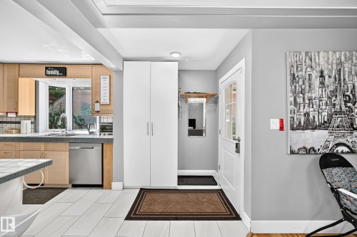 Recessed lighting, wood-finish cabinetry, stainless steel dishwasher, white tile flooring, and a white paneled entry door - 10139 74 Street Nw, Edmonton, AB 