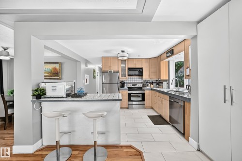 Kitchen featuring wood-finish cabinetry, stainless steel appliances, tile flooring, and a breakfast bar - 10139 74 Street Nw, Edmonton, AB 