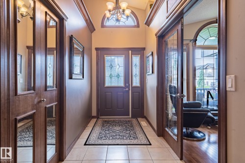 Entryway featuring an arched decorative transom window, leaded glass entry door with side lights, and overhead chandelier - 19 Newton Place, St. Albert, AB 