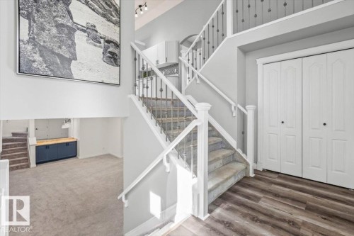 Two-story foyer featuring wood-finish flooring and a carpeted staircase with white railings and wrought iron balusters - 15420 44 Street Nw, Edmonton, AB 
