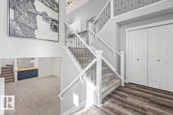 Two-story foyer featuring wood-finish flooring and a carpeted staircase with white railings and wrought iron balusters - 