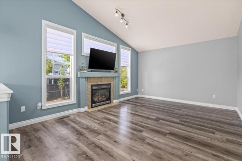 Vaulted ceiling with track lighting, wood-finish flooring, and a fireplace with a stone surround - 15420 44 Street Nw, Edmonton, AB 