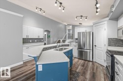 Kitchen featuring wood-finish flooring, white cabinetry, a contrasting blue island with a double basin sink, stainless steel appliances, and a mosaic tile backsplash - 