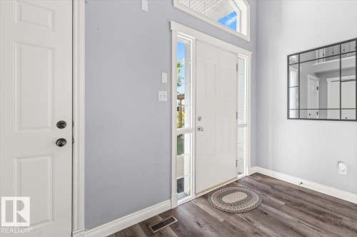 Entryway featuring wood-finish flooring, white trim, and a white paneled front door with sidelights and an arched transom window - 15420 44 Street Nw, Edmonton, AB 