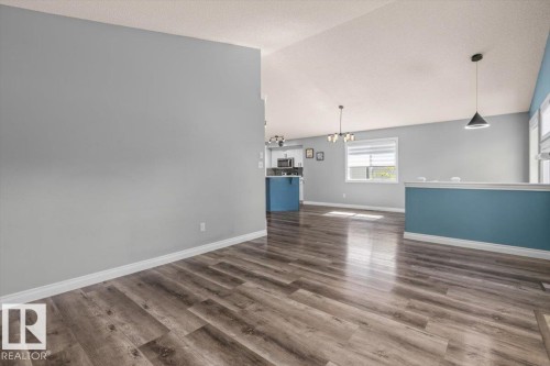 Wood-finish flooring, half-height wall with accent color, contemporary pendant lighting, and multiple windows with blinds - 15420 44 Street Nw, Edmonton, AB 