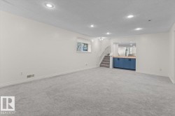 Spacious room with recessed lighting, plush carpeting, a built-in wet bar with wood-finish countertop and blue cabinetry, and a carpeted staircase with a white railing - 