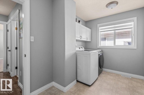 Laundry area featuring white cabinetry, light-colored flooring, and a window for natural light - 15420 44 Street Nw, Edmonton, AB 