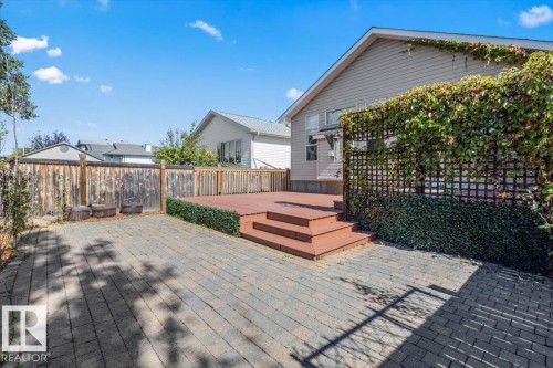 Expansive paved patio with a wooden privacy fence, multi-level wood deck, and a trellis covered with climbing greenery - 15420 44 Street Nw, Edmonton, AB 