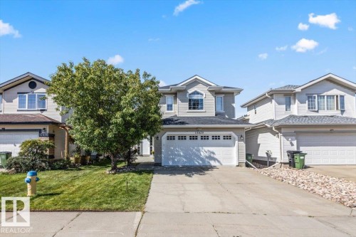 Two-story residence featuring light gray siding, a two-car garage, and an arched window - 15420 44 Street Nw, Edmonton, AB 