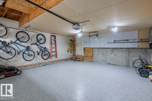 Attached garage featuring a durable epoxy floor finish, exposed wood ceiling joists, and overhead lighting - 15420 44 Street Nw, Edmonton, AB 
