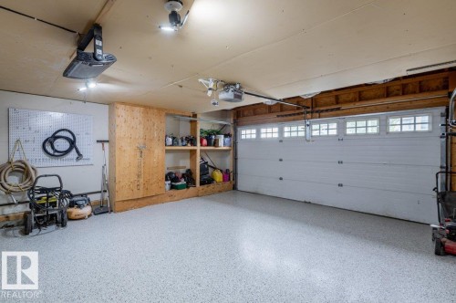 Garage featuring a white segmented door with transom windows, built-in wooden shelving, and a light-toned finished floor - 15420 44 Street Nw, Edmonton, AB 