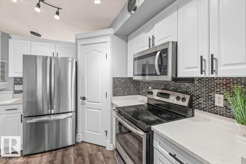 White cabinetry with black hardware, stainless steel appliances, dark mosaic tile backsplash, light-toned countertops, and wood-finish flooring - 15420 44 Street Nw, Edmonton, AB 