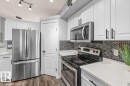 White cabinetry with black hardware, stainless steel appliances, dark mosaic tile backsplash, light-toned countertops, and wood-finish flooring - 15420 44 Street Nw, Edmonton, AB 