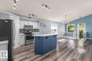 Open-concept kitchen with a contrasting blue island and white cabinetry, stainless steel appliances, and wood-finish flooring - 15420 44 Street Nw, Edmonton, AB 