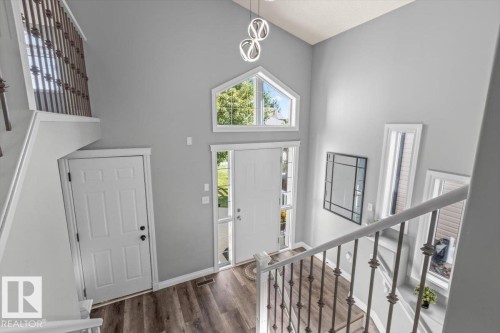 Foyer featuring vaulted ceilings, wood-finish flooring, a large entry door with sidelights, an arched transom window, and a modern chandelier - 15420 44 Street Nw, Edmonton, AB 