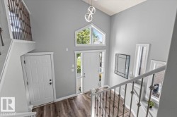 Foyer featuring vaulted ceilings, wood-finish flooring, a large entry door with sidelights, an arched transom window, and a modern chandelier - 