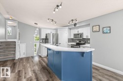 Modern kitchen with wood-finish flooring, a blue island with a white countertop, white cabinetry with stainless steel hardware, and a dark tile backsplash - 