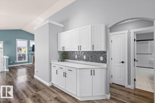 White cabinetry with black hardware, mosaic tile backsplash, wood-finish flooring, white solid core doors, and an arched doorway - 15420 44 Street Nw, Edmonton, AB 