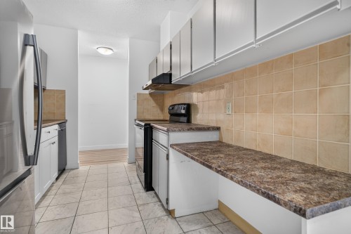 Kitchen featuring white cabinetry, tile flooring, brown tile backsplash, and dark speckled countertops - #301 9809 110 St Nw, Edmonton, AB 