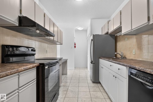 Galley kitchen featuring white cabinetry, tile flooring, tile backsplash, laminate countertops, and essential appliances - #301 9809 110 St Nw, Edmonton, AB 