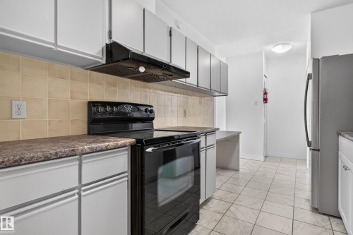 Kitchen featuring white cabinetry, a black range with an overhead vent, tiled flooring, and a stainless steel refrigerator - #301 9809 110 St Nw, Edmonton, AB 
