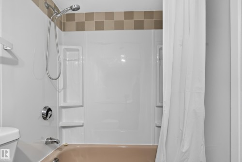 Bathtub with a shower head, polished chrome fixtures, and a tiled accent border - #301 9809 110 St Nw, Edmonton, AB 