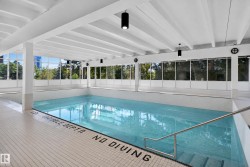 Indoor swimming pool with white tile surround, floor-to-ceiling windows, and exposed beam ceiling - 