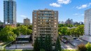 Multi-story building featuring numerous private balconies, a ground-level amenity building with expansive windows, and a paved parking area - #301 9809 110 St Nw, Edmonton, AB 
