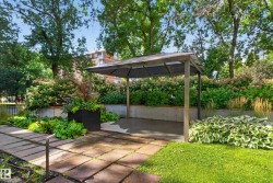 Patio area with a pergola structure, concrete paver pathway, raised garden beds, and mature landscaping - 