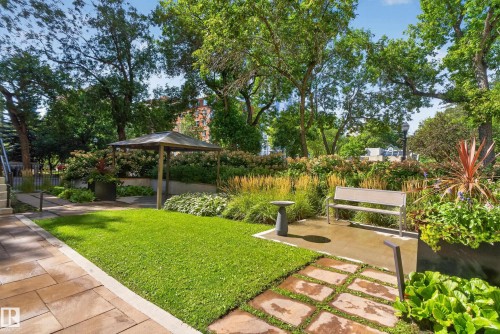 Landscaped outdoor area featuring a stone paver pathway, manicured lawn, and lush planted beds - #301 9809 110 St Nw, Edmonton, AB 