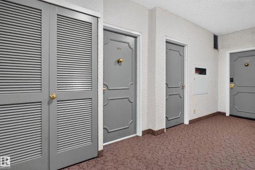 Entryway featuring patterned carpeting, textured wall finish, and multiple grey paneled doors with brass hardware - #301 9809 110 St Nw, Edmonton, AB 