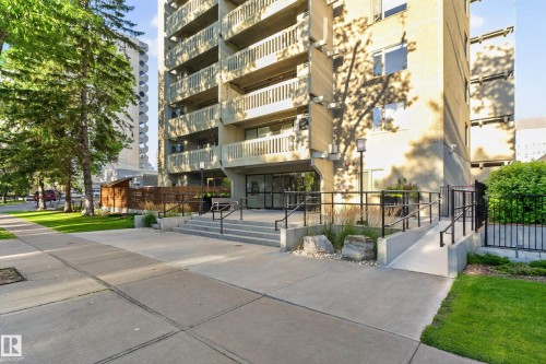 Multi-story building exterior with multiple balconies, a concrete sidewalk and steps, a pedestrian ramp with railings, and established landscaping - #301 9809 110 St Nw, Edmonton, AB 