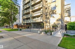 Multi-story building exterior with multiple balconies, a concrete sidewalk and steps, a pedestrian ramp with railings, and established landscaping - 