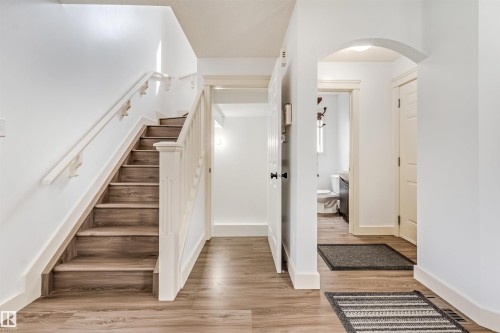 Wood-finish flooring, staircase with white railing and risers, white walls, and arched doorway - 20324 48 Avenue Nw, Edmonton, AB 