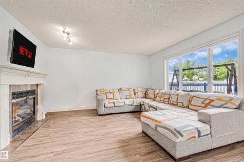 Living area with wood-finish flooring, a tiled fireplace with a white mantel, and large picture windows - 20324 48 Avenue Nw, Edmonton, AB 