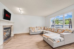 Living area with wood-finish flooring, a tiled fireplace with a white mantel, and large picture windows - 