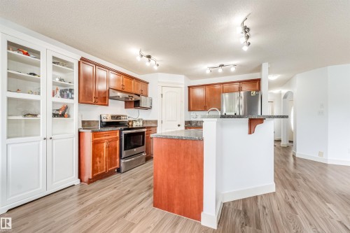 Kitchen featuring wood-finish flooring, dark wood cabinetry, stainless steel appliances, and a peninsula with a countertop - 20324 48 Avenue Nw, Edmonton, AB 