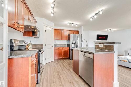 Wood-finish flooring throughout, stainless steel appliances, track lighting, and a kitchen island with an integrated sink and dishwasher - 20324 48 Avenue Nw, Edmonton, AB 