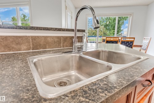 Double basin stainless steel sink with a high-arc chrome faucet, set into a speckled countertop with a tiled backsplash - 20324 48 Avenue Nw, Edmonton, AB 