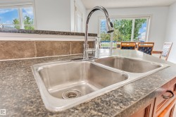 Double basin stainless steel sink with a high-arc chrome faucet, set into a speckled countertop with a tiled backsplash - 