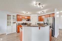 Kitchen featuring wood-finish cabinetry, built-in display cabinets, dark countertops, a stainless steel refrigerator, and track lighting - 