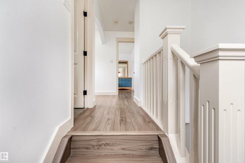 Wood-finish flooring, white painted walls, and a staircase with a detailed newel post - 20324 48 Avenue Nw, Edmonton, AB 