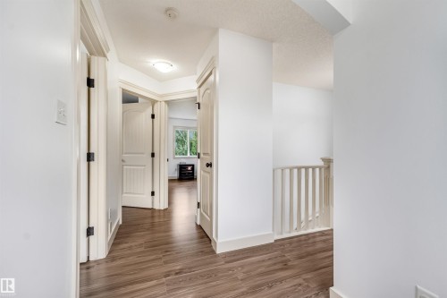 Wood-finish flooring throughout, white interior doors with dark hardware, bright white walls, and a visible stair railing - 20324 48 Avenue Nw, Edmonton, AB 