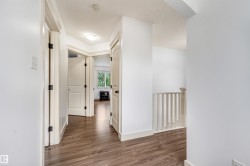 Wood-finish flooring throughout, white interior doors with dark hardware, bright white walls, and a visible stair railing - 
