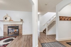 Fireplace with tile surround and mantel, wood-finish flooring, staircase with white railing, and an arched entryway - 