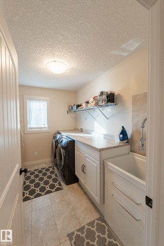 Laundry area featuring a utility sink, white cabinetry, a countertop, tiled flooring, and a window - 914 Crystallina Nera Way Nw, Edmonton, AB 